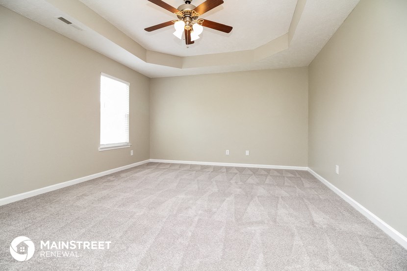 the spacious living room with carpeted flooring and a ceiling fan