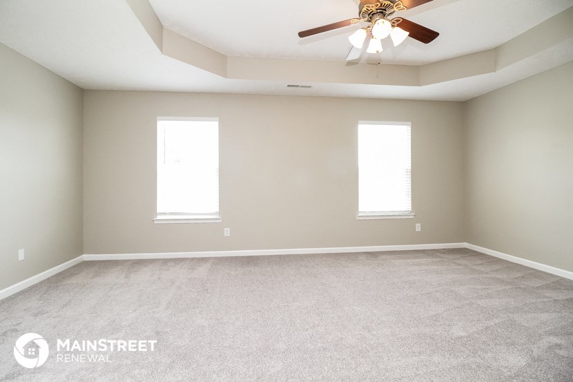 an empty room with a ceiling fan and two windows