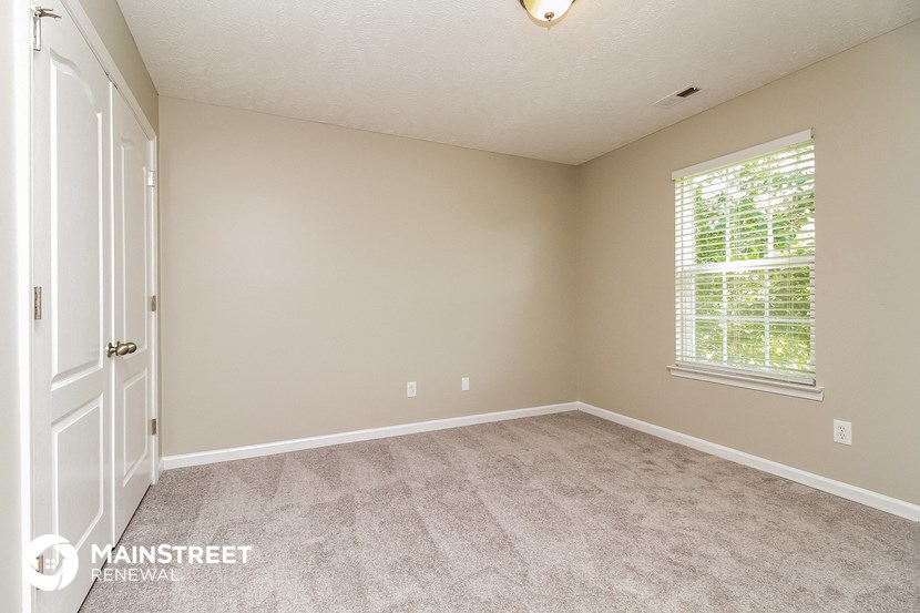 the bedroom of a house with carpet and a window