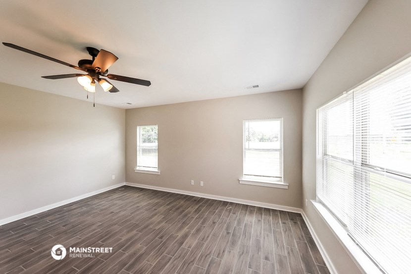 the spacious living room with wood flooring and a ceiling fan