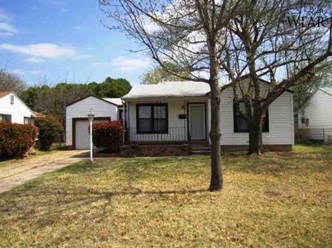 A small white house with a porch and a tree in front.