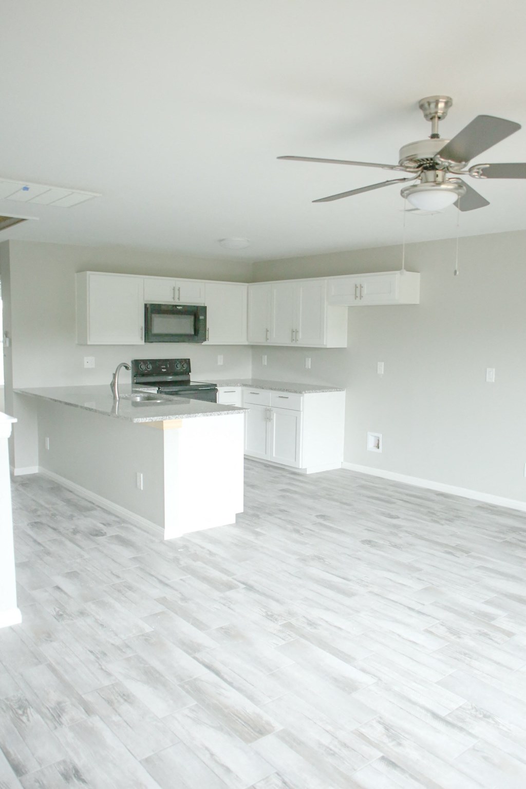 an empty kitchen and living room with white cabinets and a ceiling fan