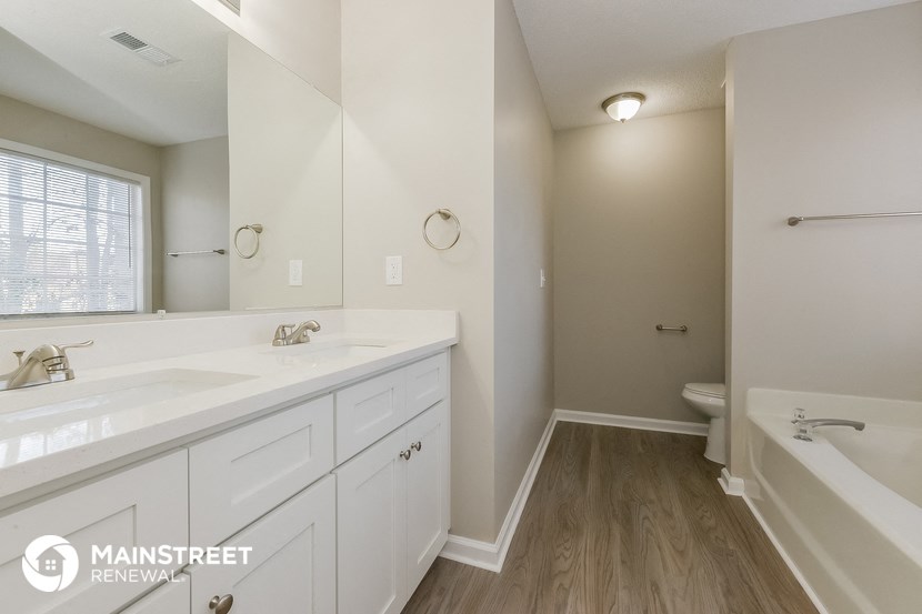 a bathroom with white cabinets and a large mirror and a tub and a sink