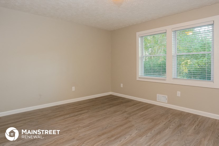 the interior of an empty room with wood flooring and two windows