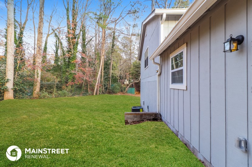 the side of a house with a lawn and trees