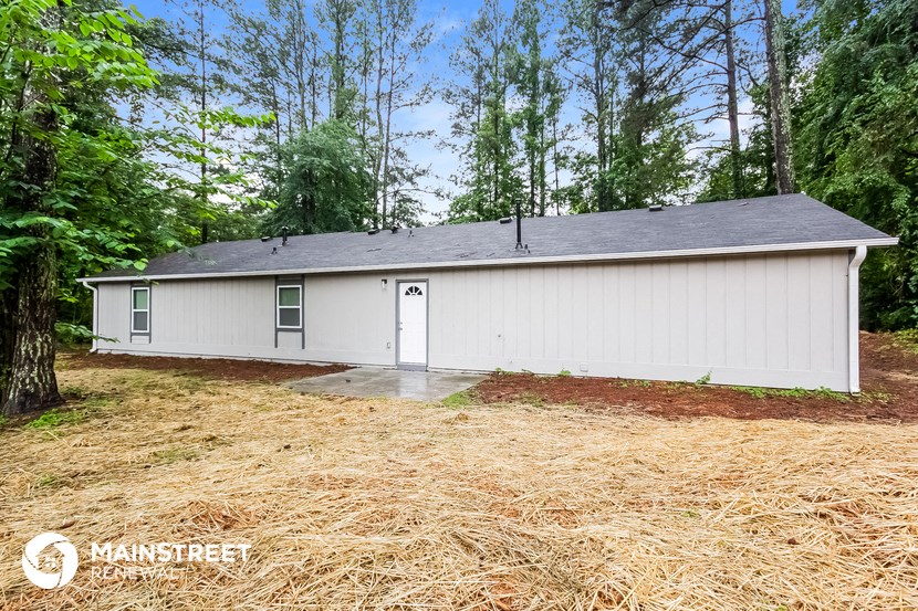 a small white house with a garage in the woods