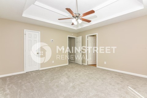 a living room with beige carpet and a ceiling fan