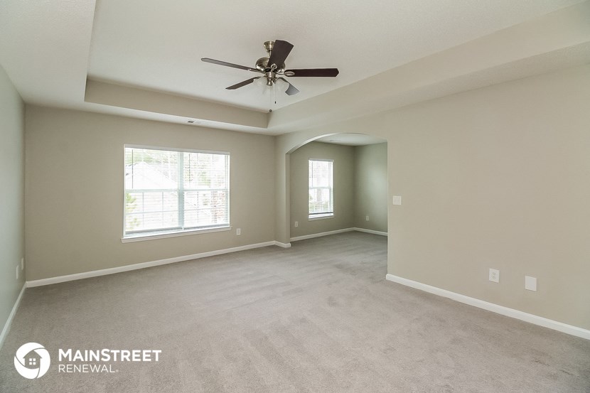 the spacious living room with ceiling fan and carpeting