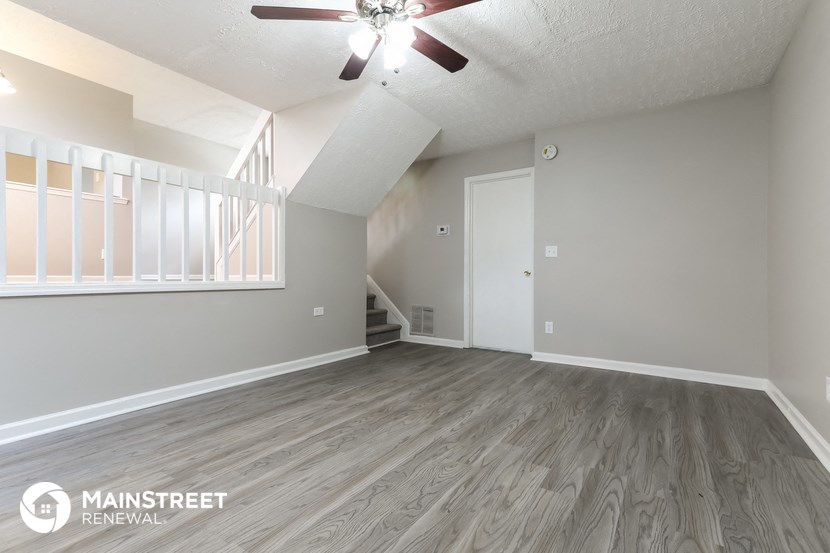 the spacious living room of an apartment with a ceiling fan
