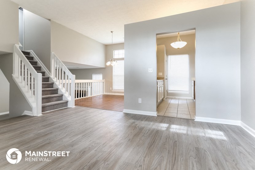 an empty living room with a staircase and a hallway to a kitchen