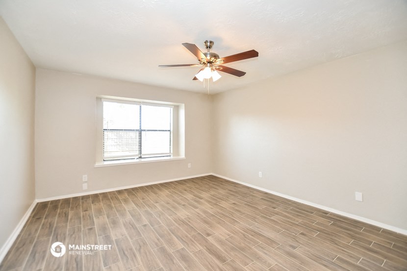 the spacious living room with wood flooring and a ceiling fan