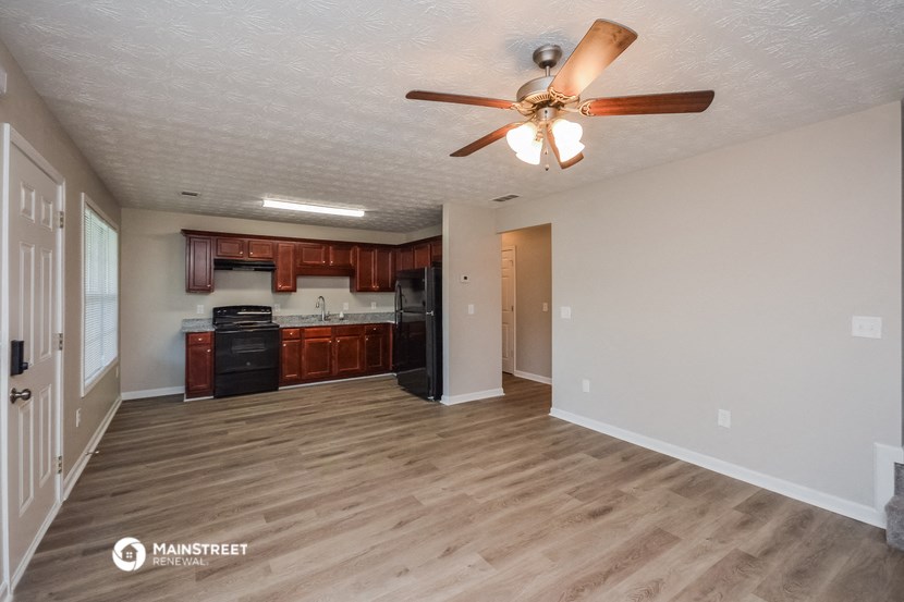 an empty living room with a ceiling fan and a kitchen