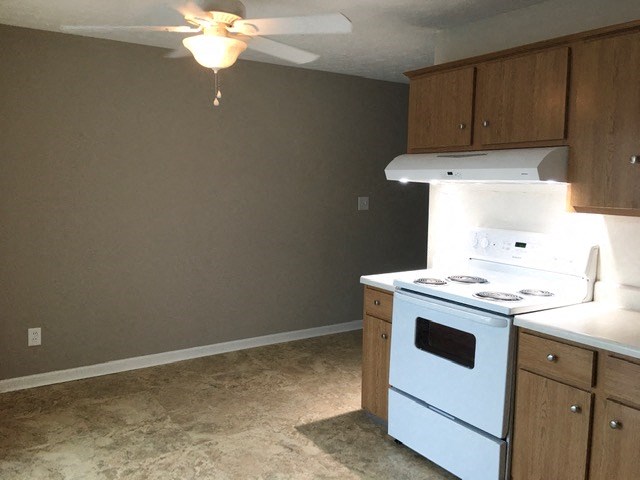 an empty kitchen with a white stove and a ceiling fan
