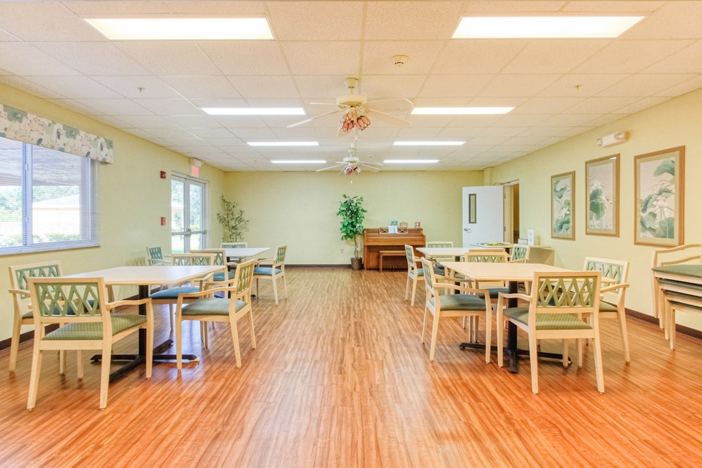 Community room with tables, chairs, piano, and plenty of light