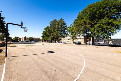 an empty basketball court in a parking lot with trees