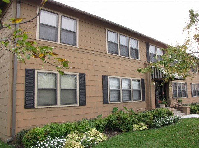a brown house with black window shutters and a garden
