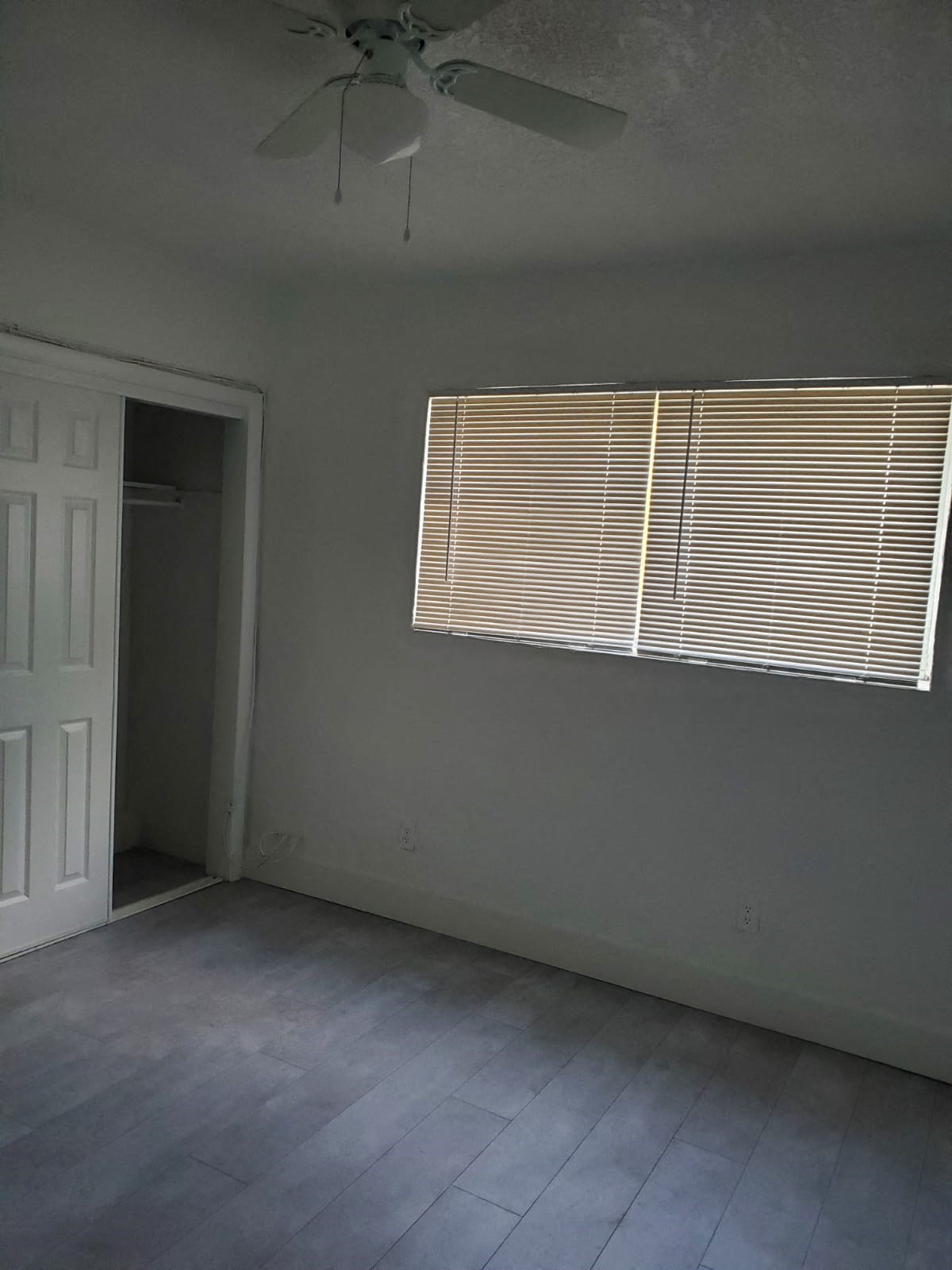 A room with a ceiling fan and a window with blinds.