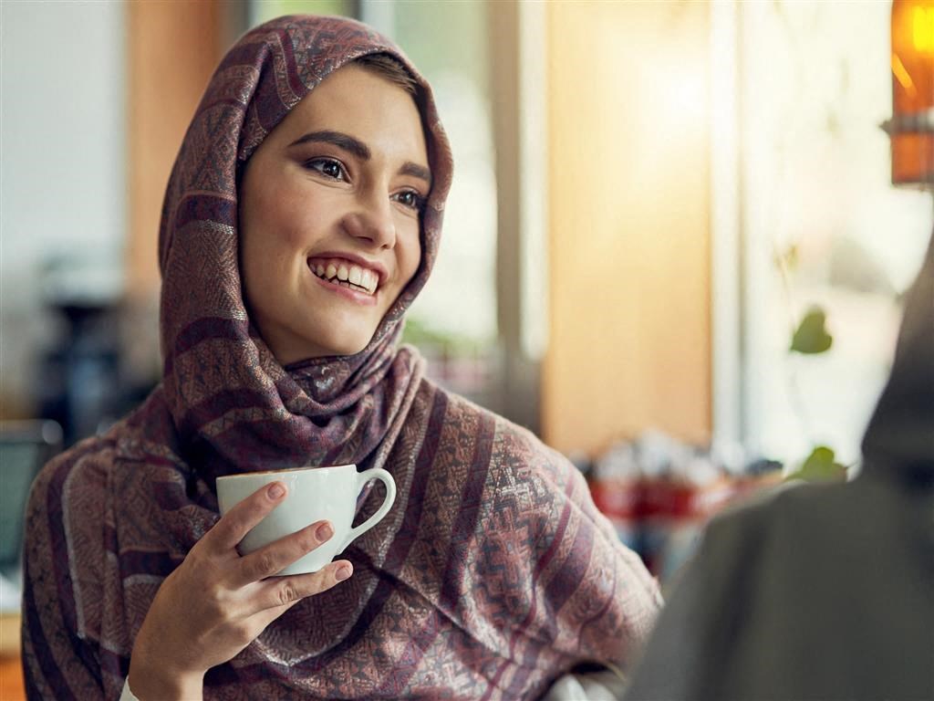 a woman holding a cup of coffee and looking at a laptop
