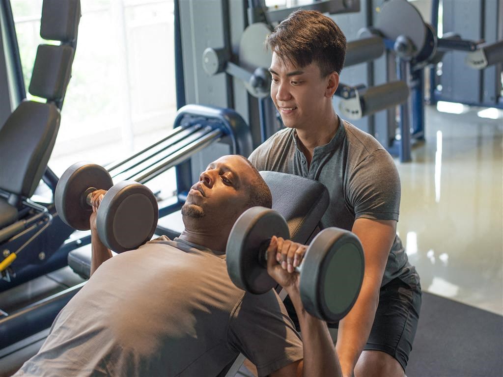 a man lifting weights with a trainer in a gym