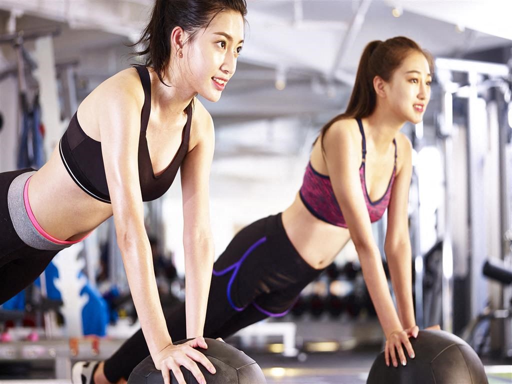 two women doing pushups on a ball in a gym