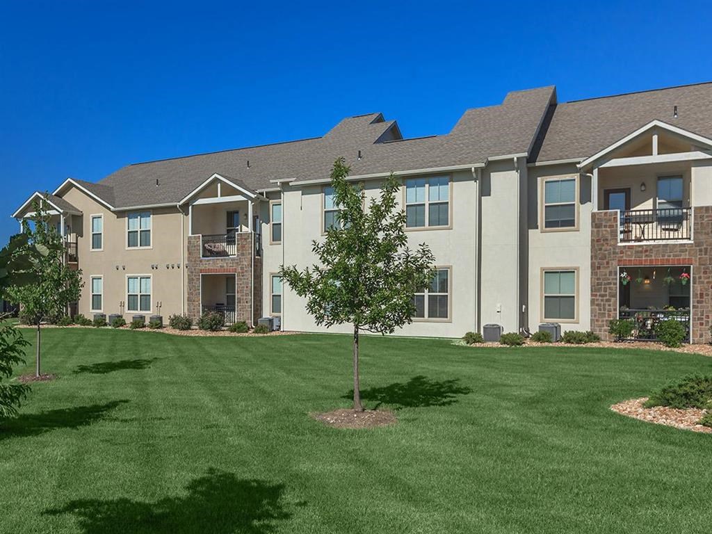 an apartment building with a lawn and a tree in front of it