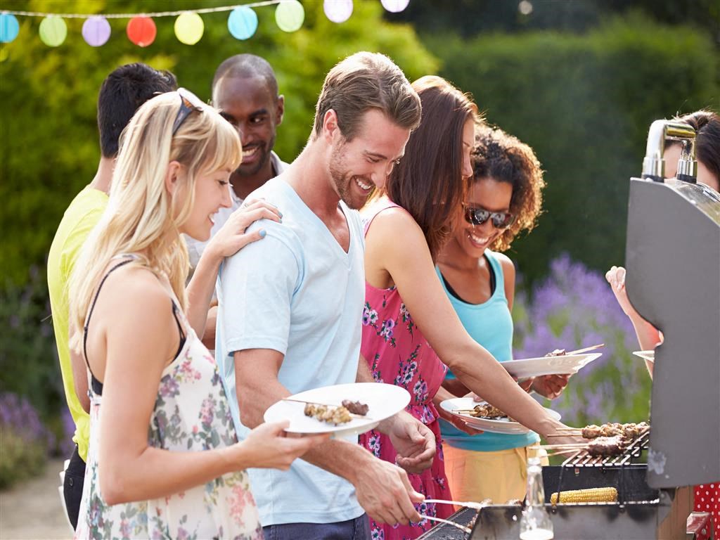 a group of people standing around a barbeque with food