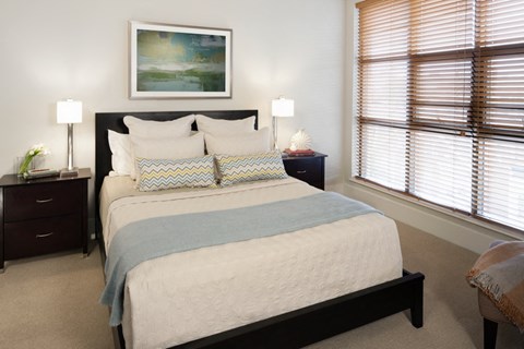 a bedroom with a bed and two nightstands and two windows