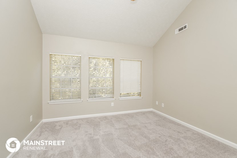 the spacious living room with three windows and carpeted flooring
