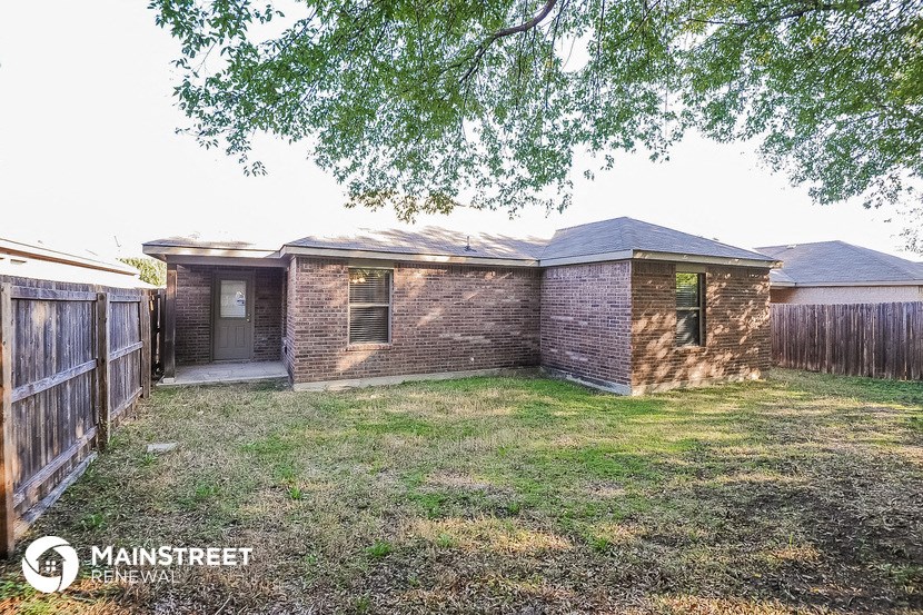 a small brick house with a yard and a wooden fence