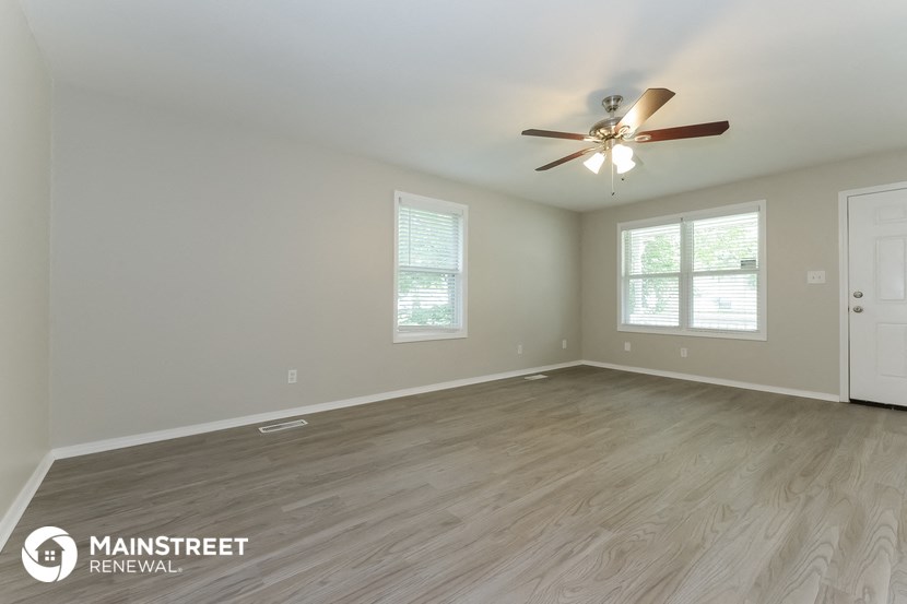 the spacious living room with wood flooring and a ceiling fan