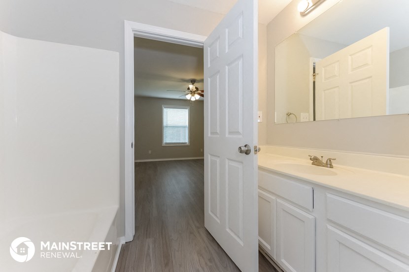 a bathroom with white cabinets and a sink and a hallway with a door to a