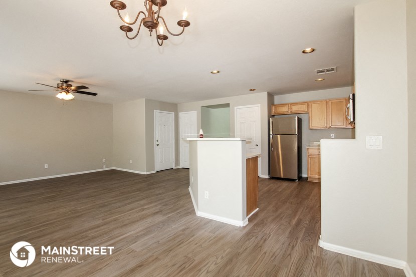 the living room and kitchen of an apartment with wood floors and a ceiling fan