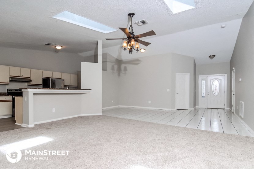 an empty living room with a ceiling fan and a kitchen