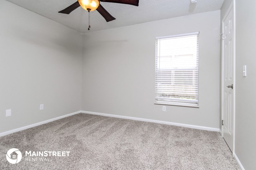 the spacious bedroom with carpeted flooring and a ceiling fan