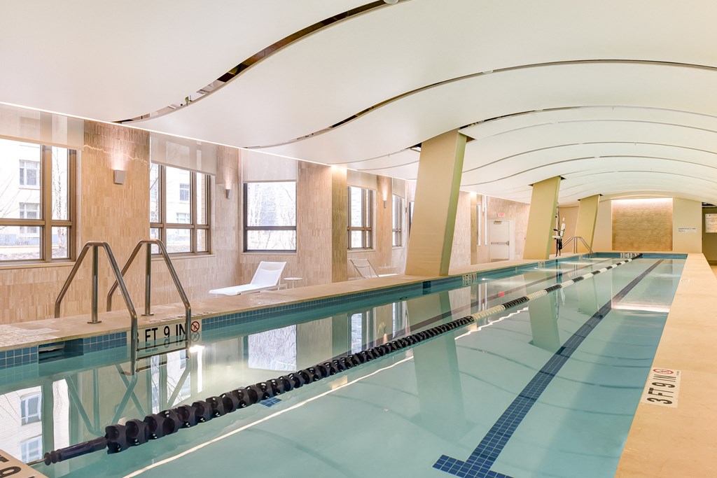 a swimming pool in a building with wood floors and white chairs