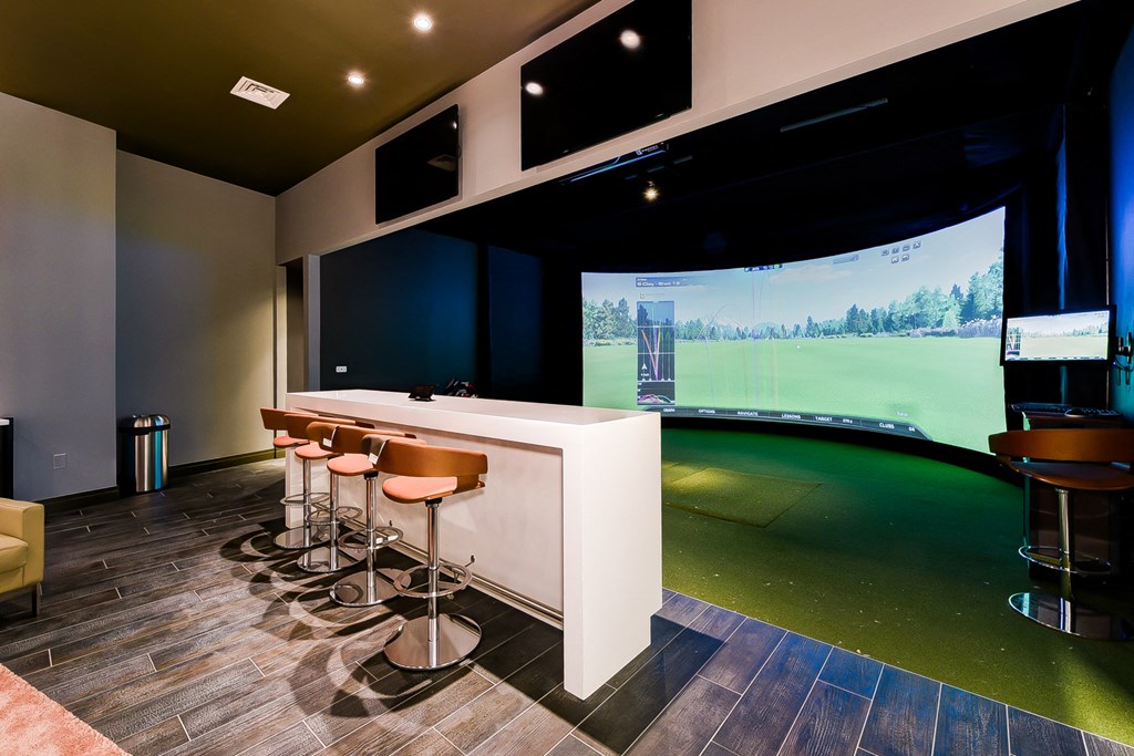 a bar with stools in front of a golf simulator in a room with a