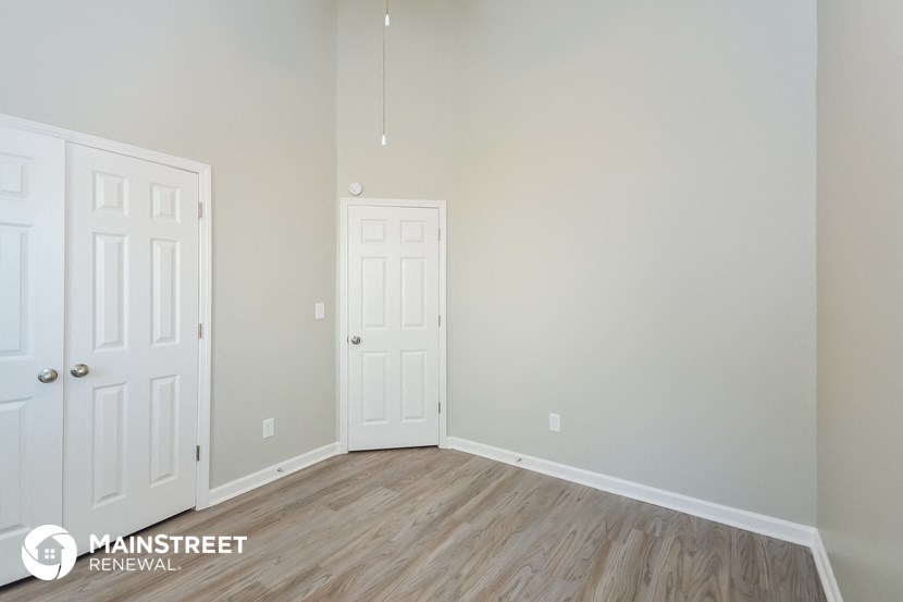 the living room of a home with white doors and wood flooring