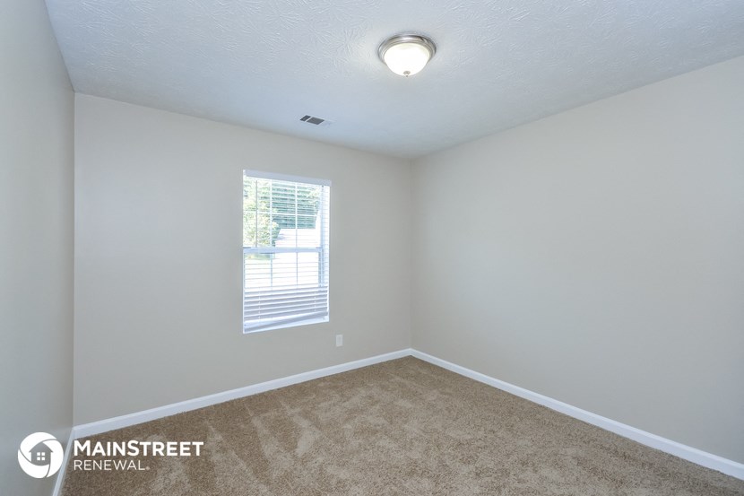 the living room of an apartment with carpet and a window