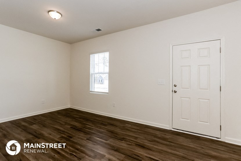 the spacious living room with white walls and wood flooring