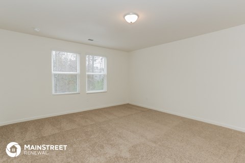 the spacious living room of a home with carpet and two windows