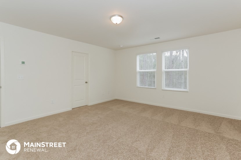 a spacious living room with carpet and two windows