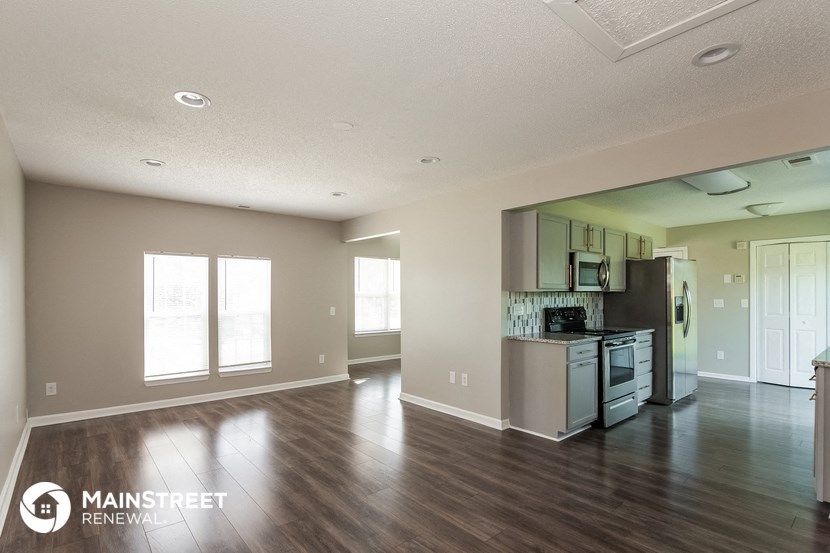 an empty living room and kitchen with wood flooring and stainless steel appliances