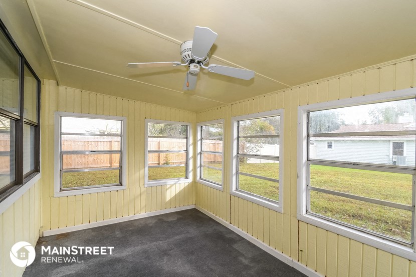 the screened porch has a ceiling fan and large windows