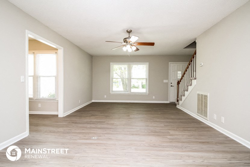 an empty living room with a ceiling fan and a staircase