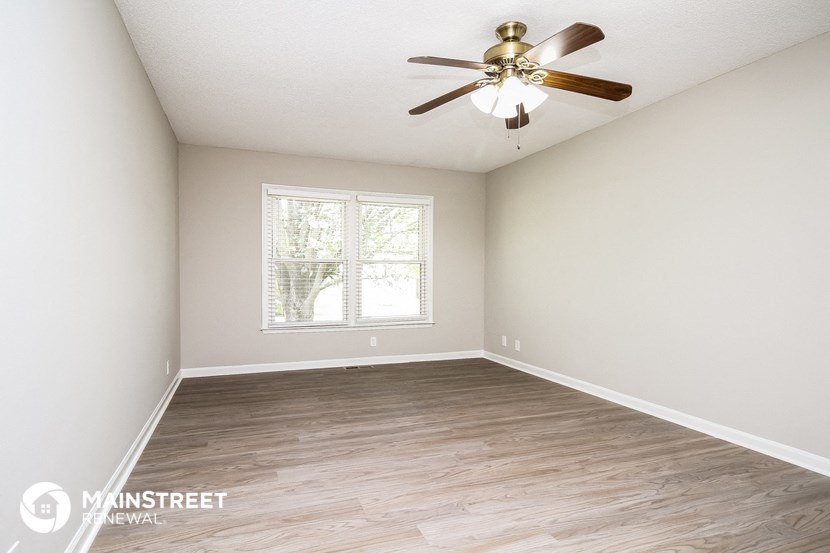 the spacious living room with wood flooring and a ceiling fan