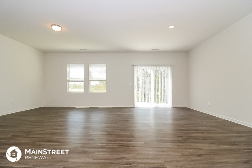 the spacious living room with wood floors and white walls