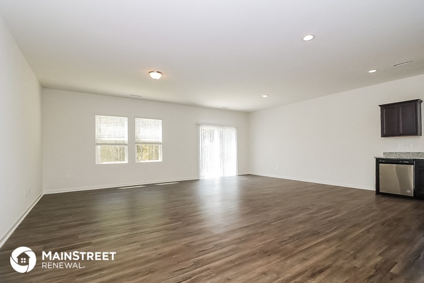 the spacious living room with wood flooring and white walls