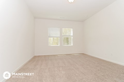 a spacious living room with carpet and two windows