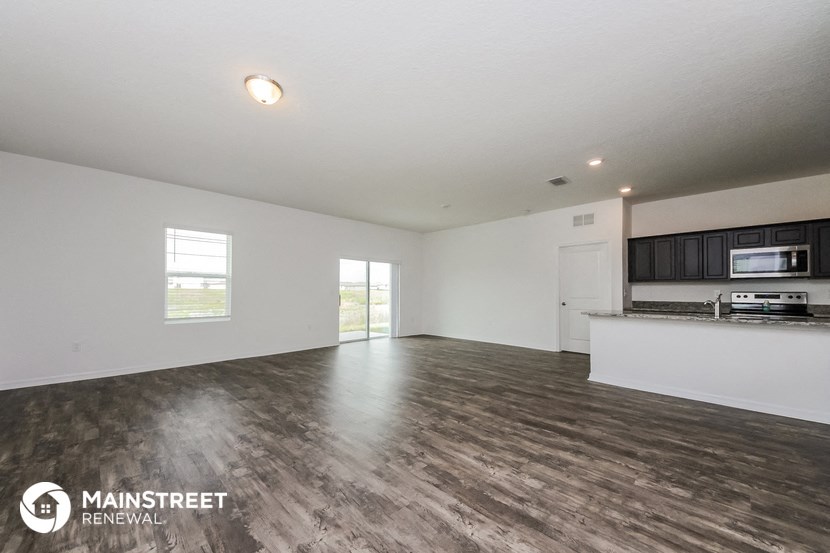 the living room and kitchen of an apartment with white walls and wood flooring