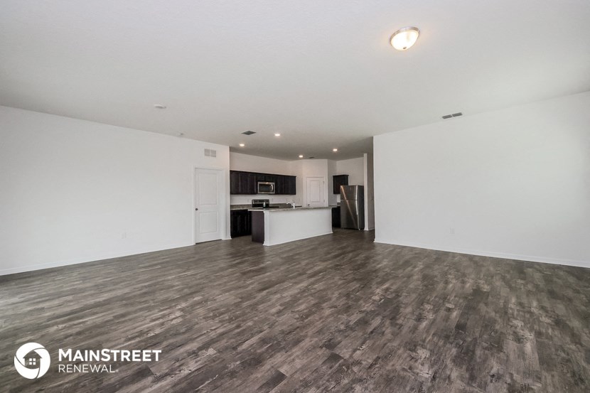 the living room and kitchen of an apartment with white walls and wood flooring